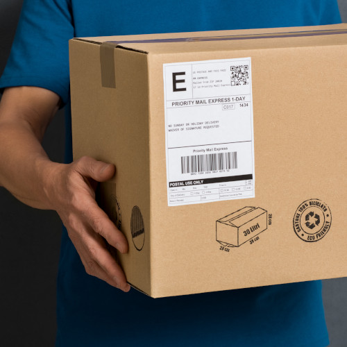 Closeup hands of delivery man holding package to deliver. Courier hand holding brown box isolated on grey background. Detail of delivery man carrying cardboard parcel with label with copy space."r